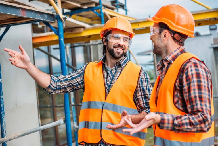 Happy builders in reflective vest and hard hat pointing at building house.jpg