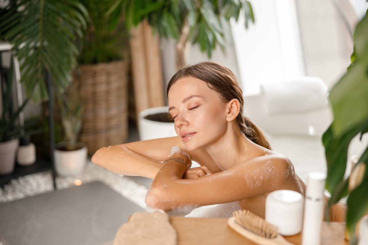 Relaxed young woman leaning on bathtub side while bathing with eyes closed at spa resort.jpg